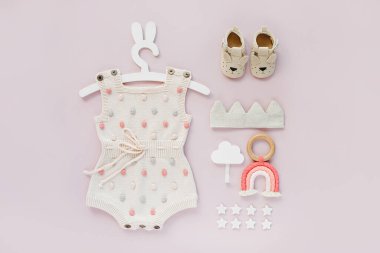 Set of baby clothes and accessories on pink background. Knitted romper with dots on cute hanger with bunny ears and shoes, cotton crown and toys. Fashion newborn. Flat lay, top view