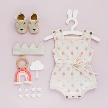 Set of baby clothes and accessories on pink background. Knitted romper with dots on cute hanger with bunny ears and shoes, cotton crown and toys. Fashion newborn. Flat lay, top view clipart