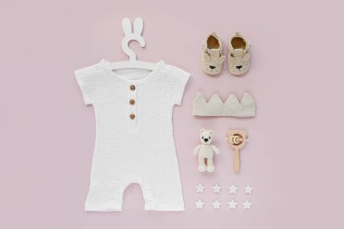 Set of baby clothes and accessories on pink background. White bodysuit on cute hanger with bunny ears and shoes, cotton crown and toys. Fashion newborn. Flat lay, top view