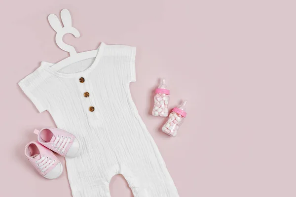 Set of baby clothes and accessories on pink background. White bodysuit on cute hanger with bunny ears and baby shoes and toys. Fashion newborn clothes. Flat lay, top view