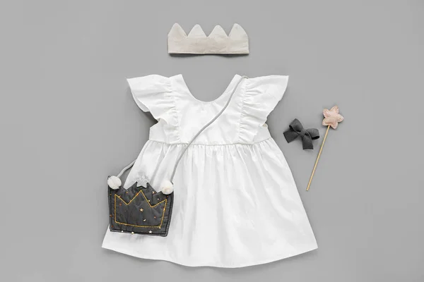 White dress, kids handbag  with cotton crown and magic wand. Set of  baby clothes and accessories for birthday on gray background. Fashion childs outfit. Flat lay, top view