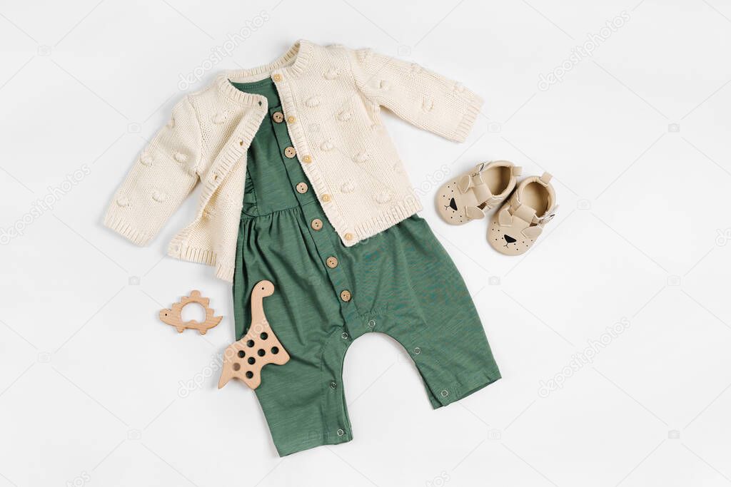 Knitted  jumper  with green romper, wooden toys and baby shoes. Set of baby clothes and accessories for little girl on white background.  Fashion newborn. Flat lay, top view