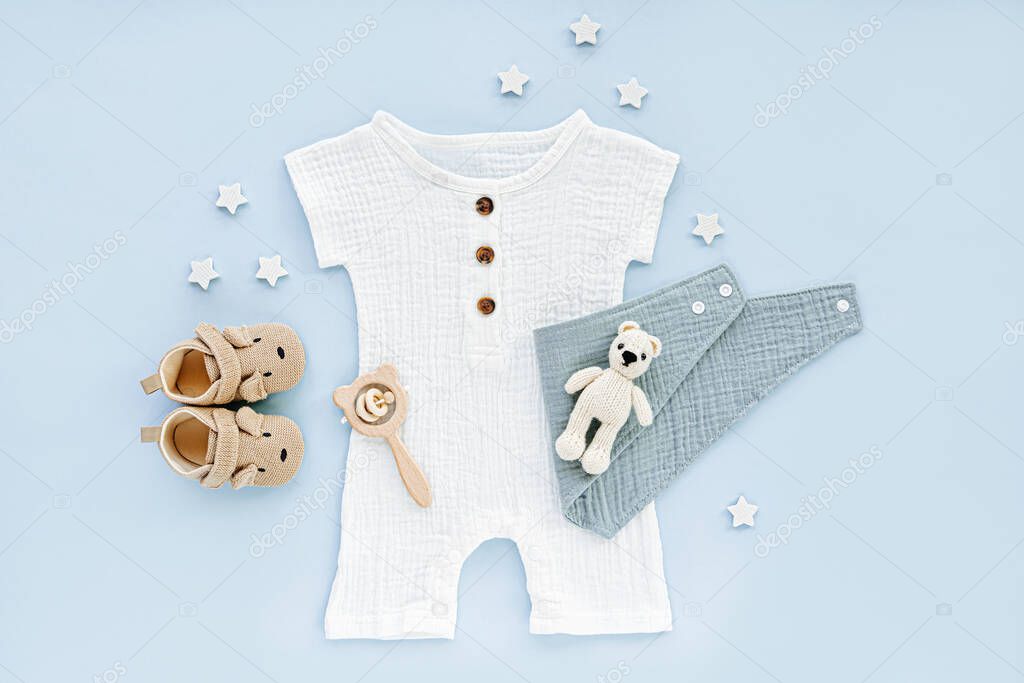 White cotton bodysuit with baby shoes and toys. Set of baby clothes and accessories on blue background. Fashion newborn clothes for summer. Flat lay, top view