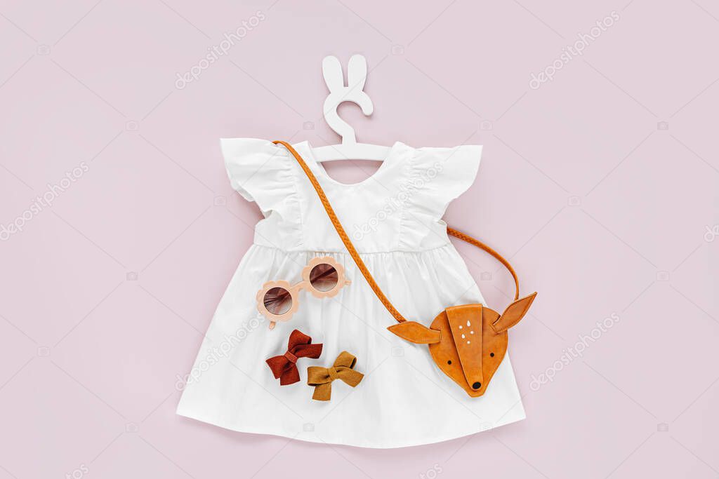 White dress  with kids handbag and sunglasses. Set of  baby clothes and accessories for spring or summer on pale pink background. Fashion childs outfit. Flat lay, top view