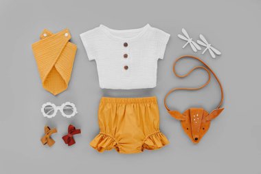 White shirt, orange shorts with kids handbag and sunglasses. Set of  baby clothes and accessories for summer vacation on  gray background. Fashion childs outfit. Flat lay, top view