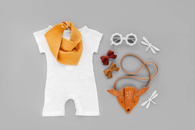 White romper, orange bib with kids handbag and sunglasses. Set of  baby clothes and accessories for summer vacation on  gray background. Fashion childs outfit. Flat lay, top view
