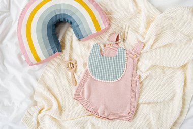 Pink bodysuit and  bib on knitted blanket. Set of  kids clothes and accessories  on bed. Fashion newborn. Flat lay, top view