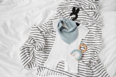 White romper and blue bib with baby toys. Set of  kids clothes and accessories for summer  on  bed. Fashion childs outfit. Flat lay, top view