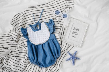 Blue  baby dress with bib, sunglasses and photo frame. Set of  kids clothes and accessories for summer vacation on  bed. Fashion newborn. Flat lay, top view