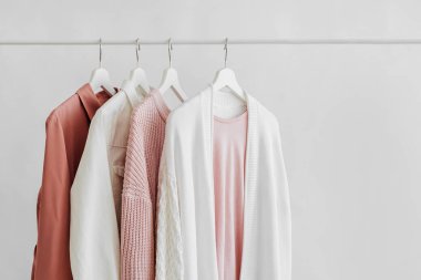 Feminine clothes in pastel pink  color on hanger on white background.  Elegant dress,  jumper, shirt and other fashion outfit. Spring cleaning home wardrobe. Minimal concept.