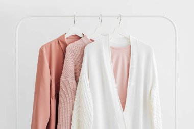 Feminine clothes in pastel pink  color on hanger on white background.  Elegant dress,  jumper, shirt and other fashion outfit. Spring cleaning home wardrobe. Minimal concept.