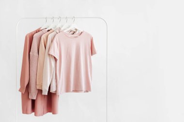 Feminine clothes in pastel pink  color on hanger on white background.  Elegant dress,  jumper, shirt and other fashion outfit. Spring cleaning home wardrobe. Minimal concept.