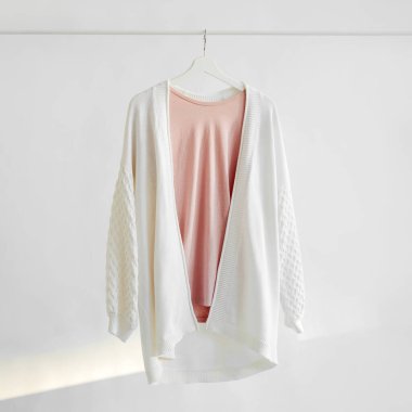 Elegant white jumper with pastel pink t-shirt  on hanger on white background. Spring  outfit.  Minimalist Feminine clothes.