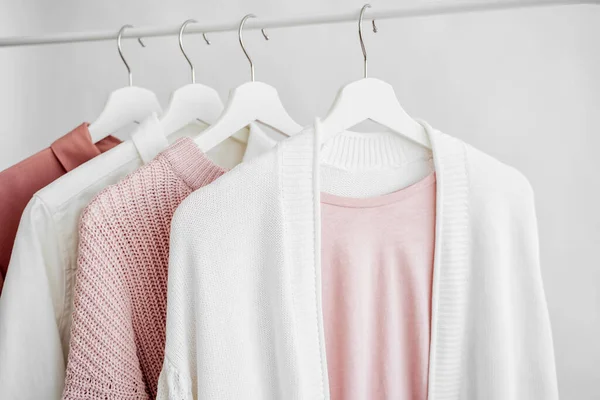 Feminine clothes in pastel pink  color on hanger on white background.  Elegant dress,  jumper, shirt and other fashion outfit. Spring cleaning home wardrobe. Minimal concept.