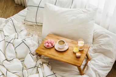 Yatakta ki tahta kahve tepsisi ve mumlar. Çizgili battaniye ve yastık ile beyaz yatak çarşafları. Yatakta kahvaltı. Hygge kavramı.