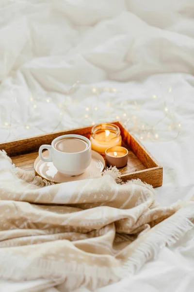 Tray of coffee and candles with warm plaid on white bedding . Breakfast in bed.  Scandinavian style.  Flat lay, top view