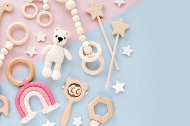 Cute wooden baby toys on pink and light-blue background. Knitted bear, rainbow, dinosaur toy, beads and stars. Eco accessories,  beanbag and teethers for newborn. Flat lay, top view