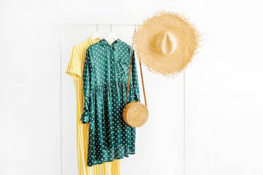 Summer dresses and straw hat with bamboo bag on hanger on white background. Elegant   fashion outfit. Spring wardrobe. Minimal concept.
