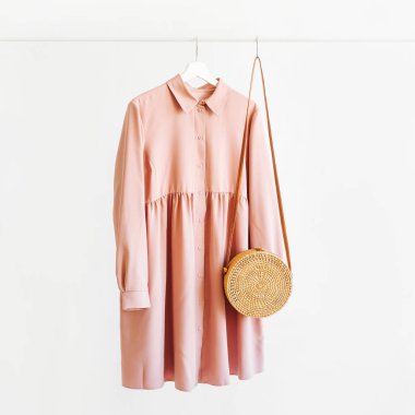 Pale pink dress with bamboo bag on hanger on white background. Elegant   fashion outfit. Spring wardrobe. Minimal concept.