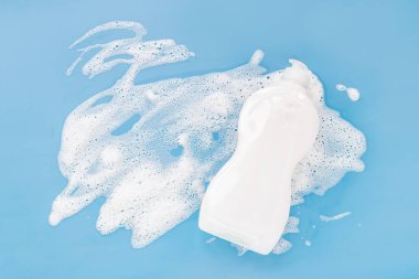 Bottle with washing agent with white soapy foam on a blue background. Cleaning/Washing concept. Flat lay, Top view.
