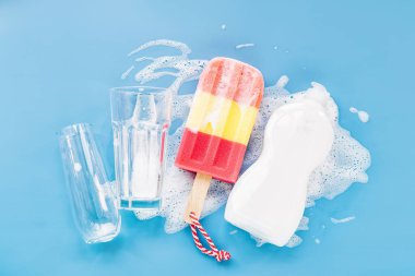 Bottle with washing agent and sponge in the form of ice cream and glass on soapy foam background. Washing dishes concept. Flat lay, Top view.