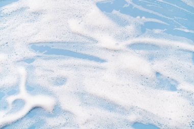 White soapy foam on a blue background. Cleaning/Washing concept