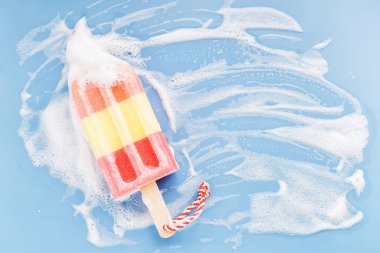 Sponge in the form of ice cream on soapy foam background. Washing dishes concept. Flat lay, Top view.