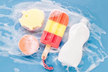 Bottle with washing agent and sponges on soapy foam background. Washing dishes concept. Flat lay, Top view.