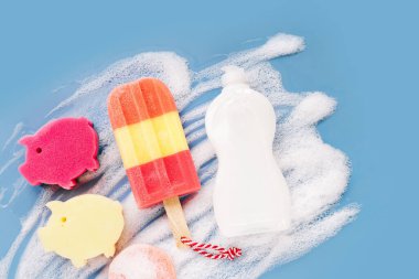 Bottle with washing agent and sponges on soapy foam background. Washing dishes concept. Flat lay, Top view.