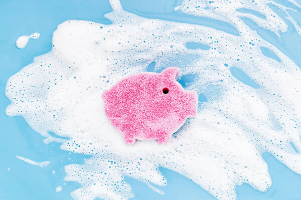 Sponge of cute pig shaped on soapy foam background. Washing dishes concept. Flat lay, Top view.