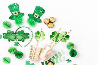 Decorations and props for St.Patrick 's Day party. Green and gold paper decorations, hat, balloons, confetti, candy and lucky symbols on white background. Festive concept. Flat lay, top view.