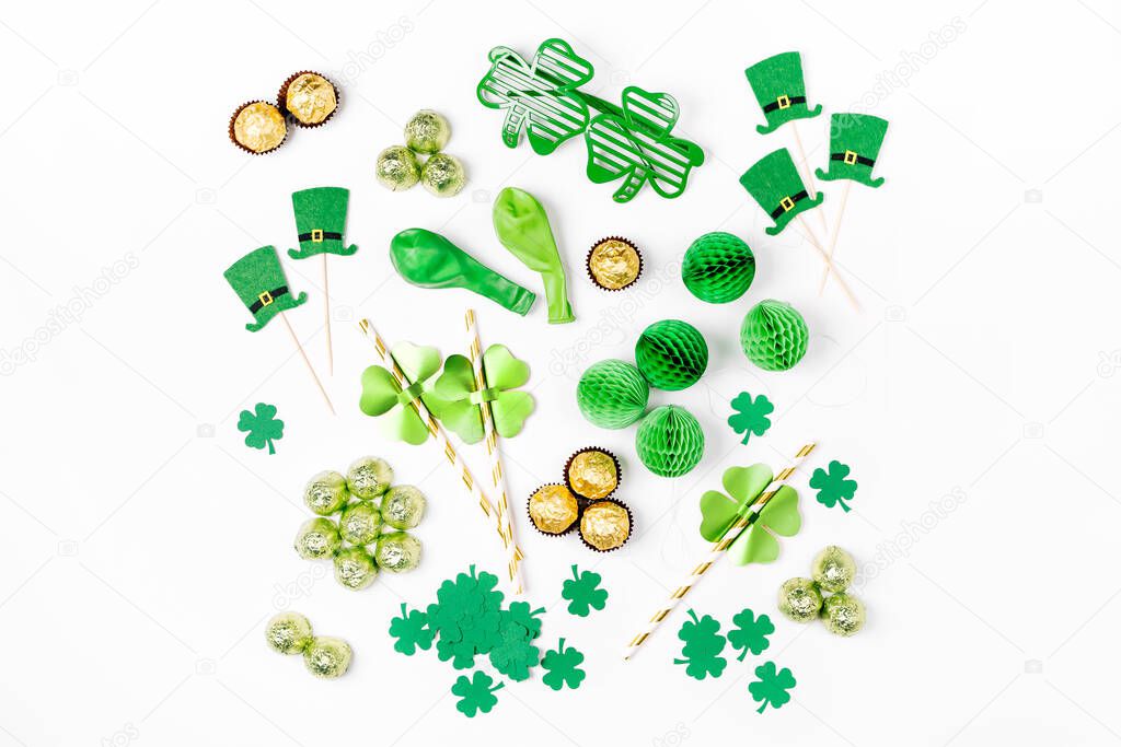 Decorations and props for St.Patrick 's Day party. Green and gold paper decorations, hat, balloons, confetti, candy and lucky symbols on white background. Festive concept. Flat lay, top view.