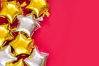 Gold and silver foil balloons of star shaped on red background. Holiday and celebration concept. Birthday Day or party decoration. Metallic air balloons. Congratulation. Greeting card. 