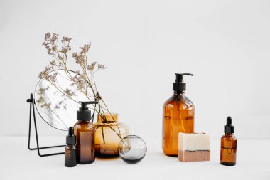Branch flowers in a glass vase, mirror,  shampoo bottles and soap on white table. Decor for interior. Stylish decoration for home.