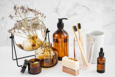 Branch flowers in a glass vase, mirror and cosmetics products  on white table. Decor for interior. Stylish decoration for home.