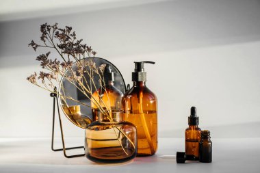Branch flowers in a glass vase, mirror and cosmetics products  on white table. Decor for interior. Stylish decoration for home.