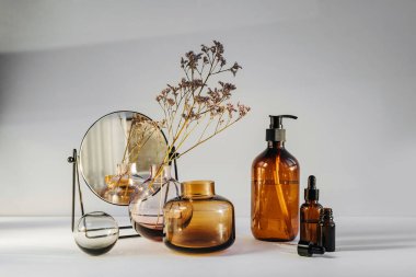 Branch flowers in a glass vase, mirror and cosmetics products  on white table. Decor for interior. Stylish decoration for home.