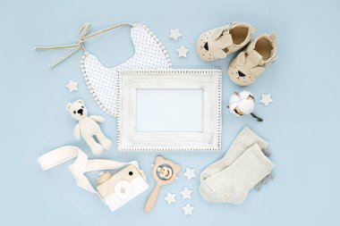 Yeni doğmuş bir çocuk için giysi ve aksesuarlı fotoğraf çerçevesi. Oyuncaklar, çoraplar ve mavi arka planda bebek terlikleri. Mesajı hazırla. Düz yatış, üst görünüm 