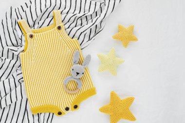 Knitted  yellow  romper and stars with toy bunny teether  for newborn on black and white blanket.  Baby stuff and accessories. Flat lay, top view clipart