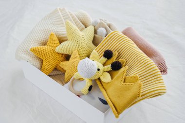 Bebek eşyaları ve yeni doğan bebek için aksesuarlarla dolu bir kutu. Örgü battaniye, giysi, çorap, ayakkabı ve oyuncak hediye kutusu. Bebek partisi konsepti. Düz yatış, üst görünüm