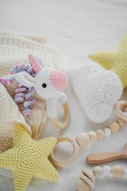 Yeni doğan bebek için beyaz yatakta örülmüş oyuncak tek boynuzlu at ve tahta ip. Bebek eşyaları ve aksesuarlar..