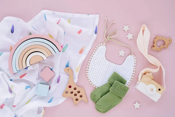 Set of clothes and accessories fot newborn. Toys, bib  and socks with muslin swaddle blanket on pink background. Baby shower concept.  Flat lay, top view