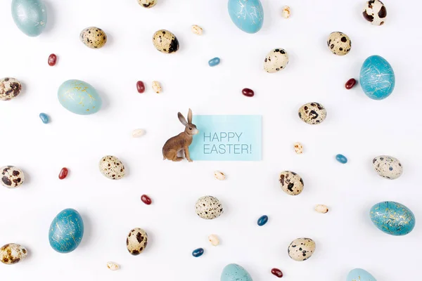 Happy Ester card. Easter bunny on white background decoration quail, gold and blue easter eggs. Flat lay, top view. Easter concept.