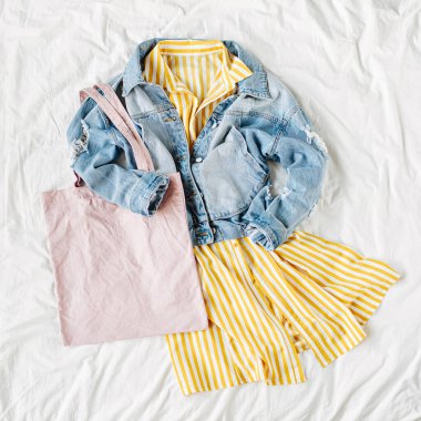 Mavi jean ceket ve beyaz yatakta eko çanta ile Sarı elbise. Kadınların şık sonbahar veya bahar kıyafeti. Modaya uygun kıyafetler. Moda konsepti. Düz döşeme, üst görünüm.