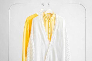 Female clothes in yellow color on hanger on white background.  Jumper and striped shirt. Spring/autumn outfit. Minimal concept.