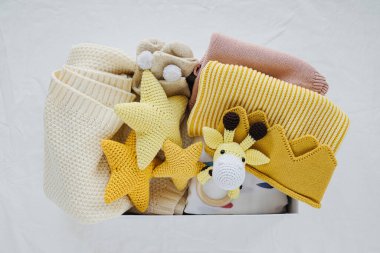Bebek eşyaları ve yeni doğan bebek için aksesuarlarla dolu bir kutu. Örgü battaniye, giysi, çorap, ayakkabı ve oyuncak hediye kutusu. Bebek partisi konsepti. Düz yatış, üst görünüm