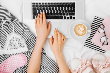 Moda blogcusu dizüstü bilgisayarla çalışıyor. Yatakta düz, üst görünümde.