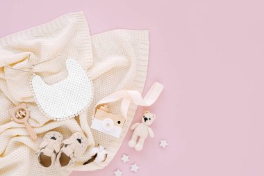Yeni doğan bebekler için giysi ve aksesuarlar. Oyuncak, önlük ve pembe arka planda örülmüş battaniyeli bebek terlikleri. Bebek partisi konsepti. Düz yatış, üst görünüm 