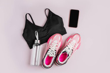 Pembe arka planda yeni spor ayakkabılar ve akıllı telefon. İçeride eğitim uygulaması. Çevrimiçi Fitness programı. Evde online antrenman. Üst manzara, düz uzanma