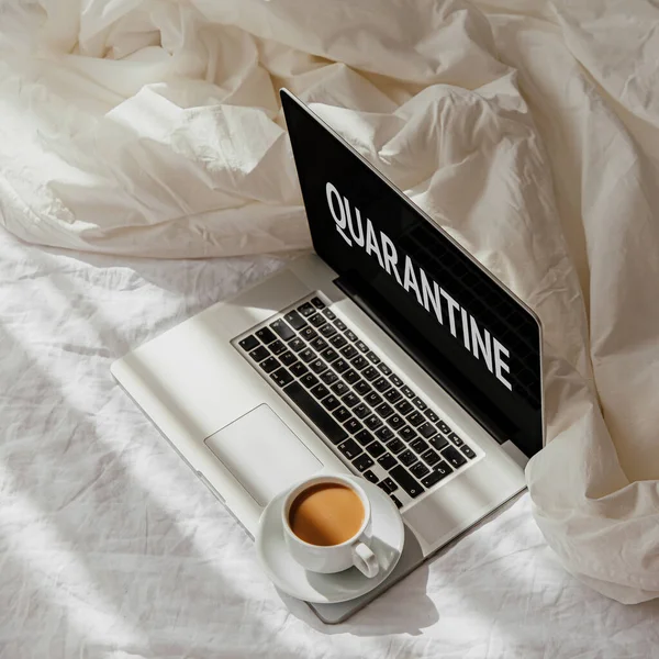 Beyaz yatakta battaniyeli dizüstü bilgisayar ve bir fincan kahve. Evde çalışma konsepti. Sabah ışığı 